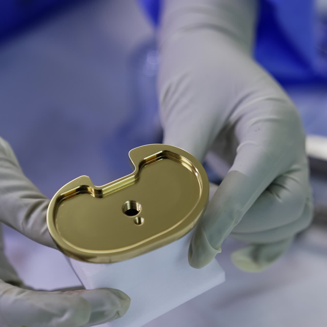 Un medico con guanti in lattice tiene delicatamente la protesi individuale di un'articolazione del ginocchio. Materiali per la moderna chirurgia endoprotesica in ospedale. Primo piano
