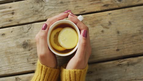 video of hands of caucasian woman holding mug with tea and lemon on wooden surface