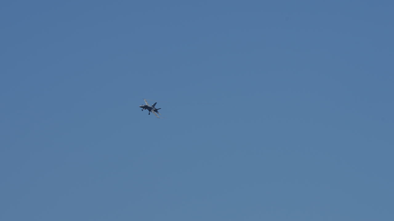 Military jet aircraft approaching with landing gear extended against clear blue sky