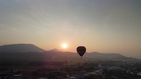 Hot-air-balloon-flying-over-a-village-with-mountainous-background-at-golden-sunrise