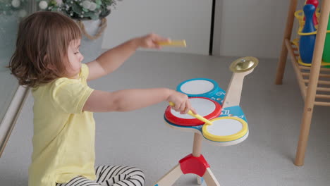 little 3-year-old girl playing drums sitting on a floor at home