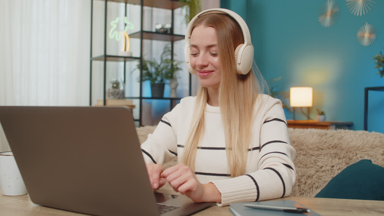 Caucasian woman listening to calming music working on laptop at home on table smiling relaxed