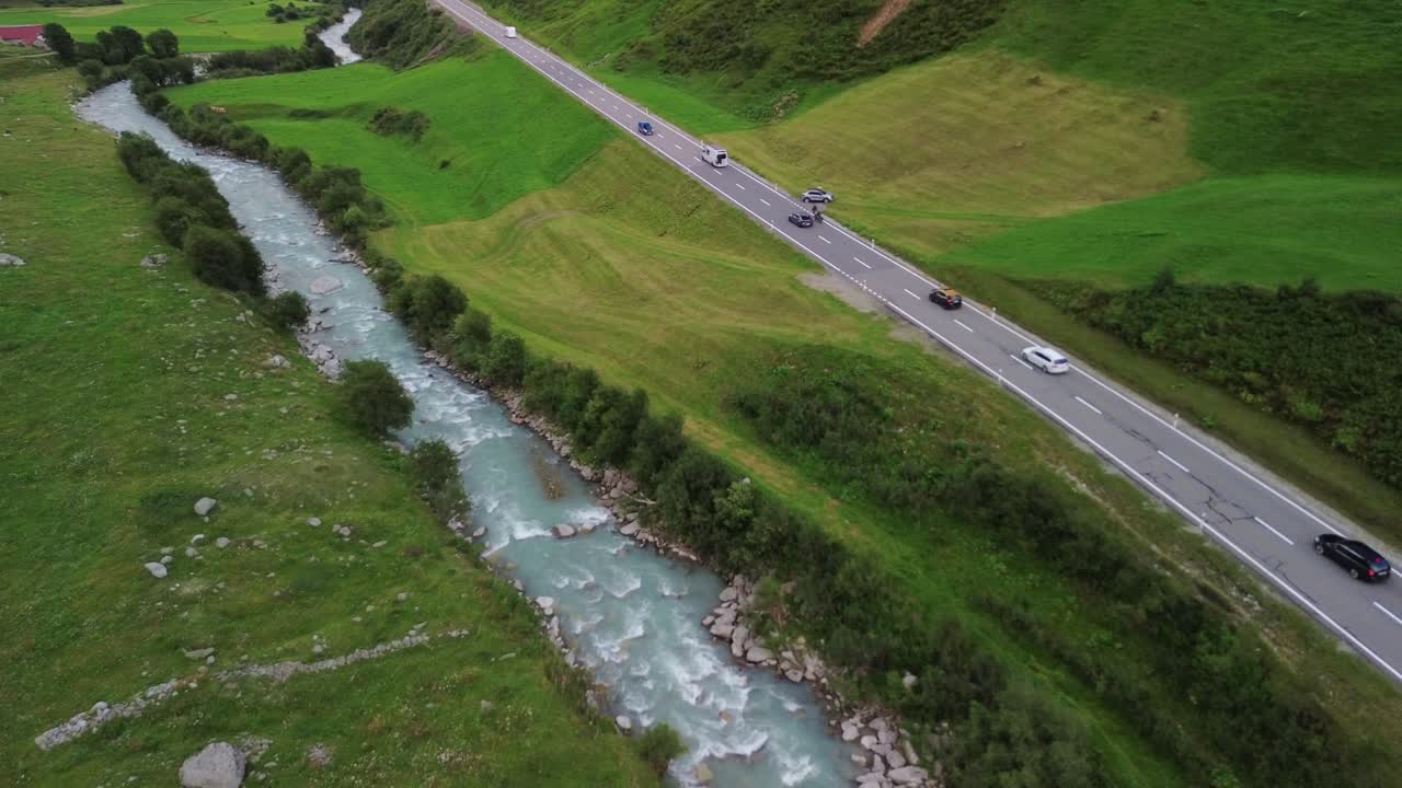 Traffic on a road in Swiss Alps with cars, cyclists andsmall stream river shot from a drone