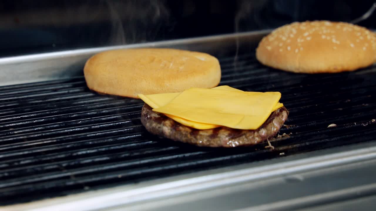Cooking delicious burger in smoke. Cheeseburger ingredients frying on a hot grill. Roasting cutlet with cheese and buns for fast food