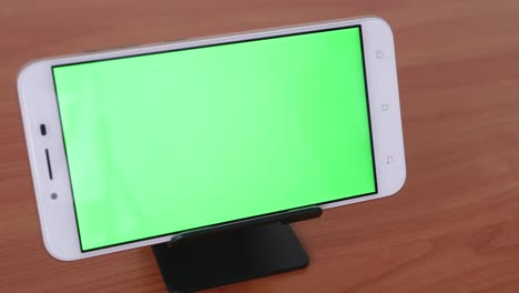 el movimiento deslizante del teléfono de pantalla verde se coloca sobre un pedestal en una mesa de madera