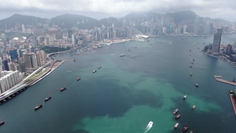 Konvoi-Lokaler-Fischerboote,-Die-In-Hongkong-Victoria-Bay-Verursachen,-Mit-Der-Skyline-Der-Stadt-Am-Horizont,-Luftbild