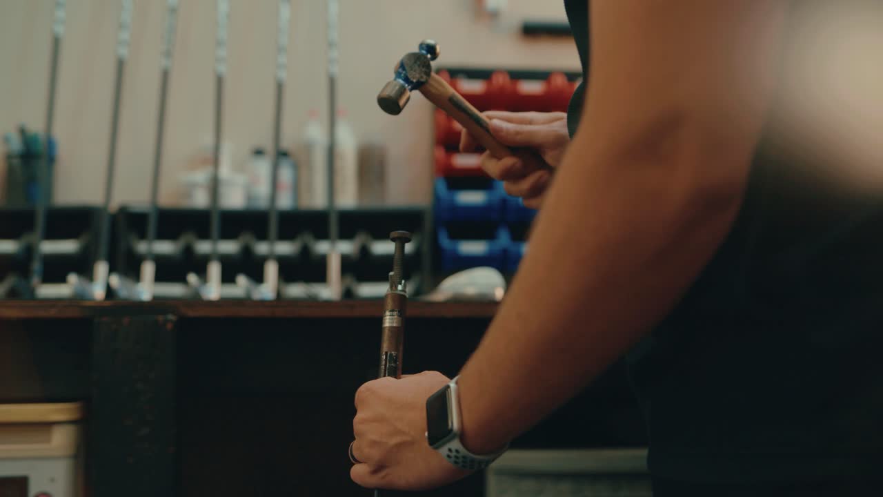 Male hands hammer nail into golf club shaft for custom fitting in workshop in slow motion