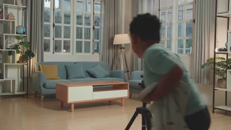asian little boy shows trick with disappearing on mobile phone camera while recording on smartphone video content for social networks in cozy room