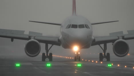 airplane is taxiing on the runway in foggy and rainy conditions, with green lights illuminating the path ahead, showcasing aviation operations