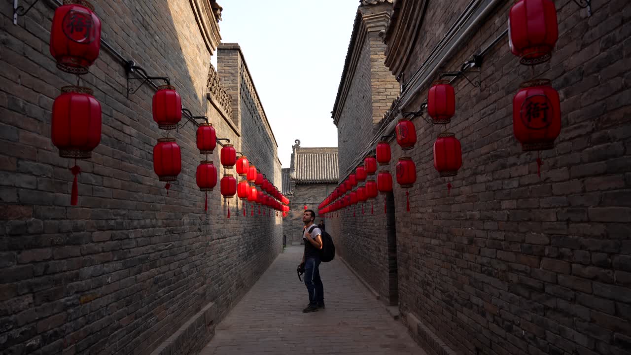 European man looking at the red lanterns of the bricked walls in Pingyao, China