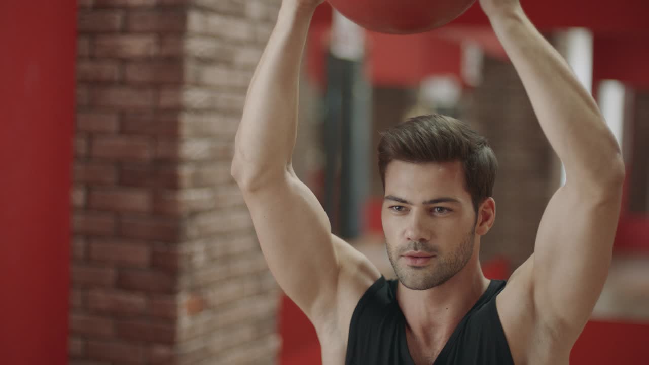 멋진 남자가 피트니스 클럽에서 공을 들고 앉아서 운동을 하고 있습니다.