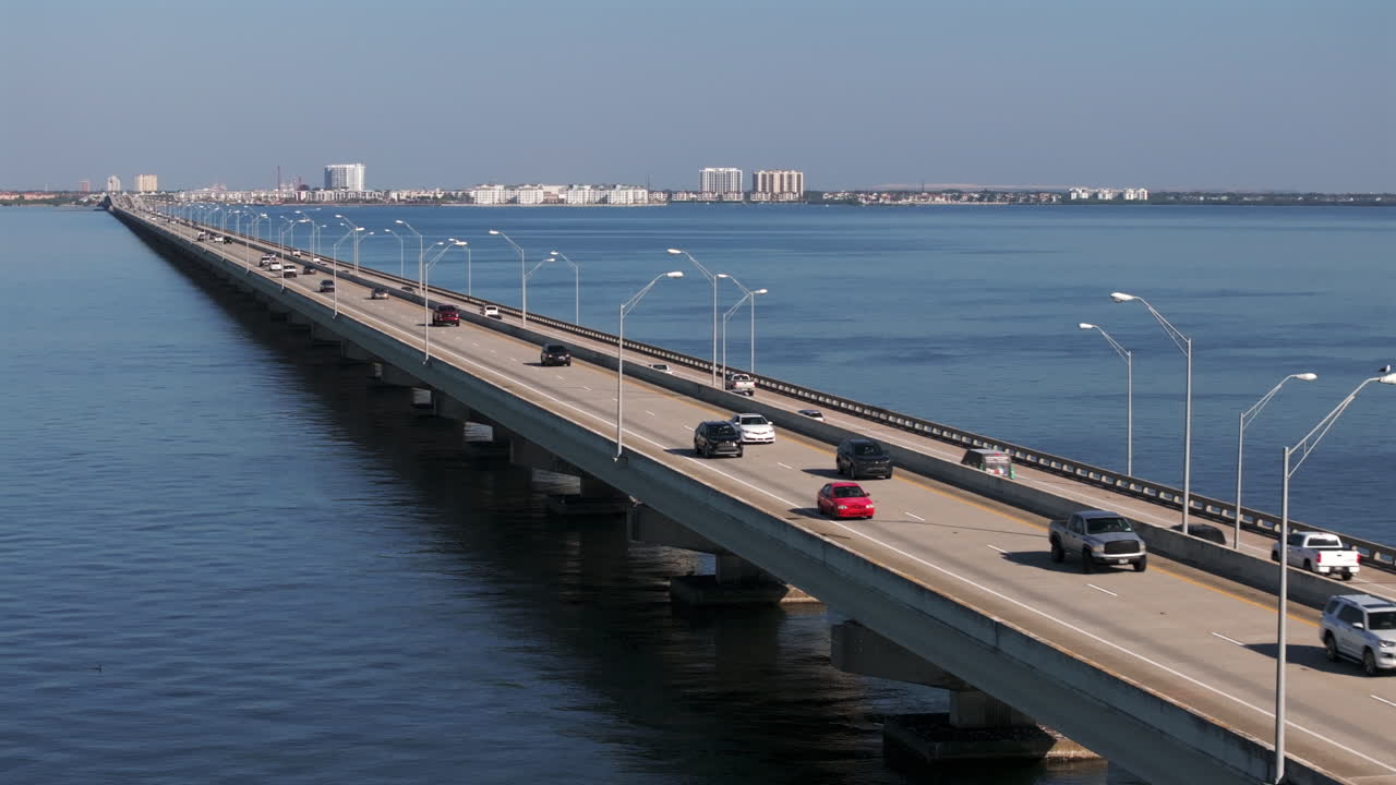 Højtliggende luftperspektiv i høj vinkel af Gandy Bridge, en større dæmning, der spænder over det vidtstrakte vand i Tampa Bay. Billedet følger den jævne strøm af køretøjstrafik på US Highway 92