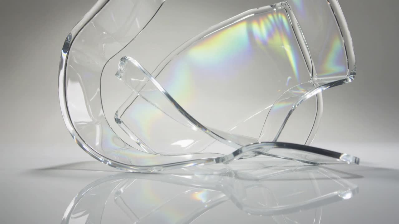 Glinting curved shards shifting on glossy studio desk after subtle light move, showing rainbow band