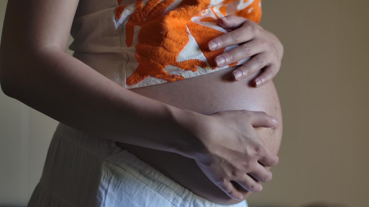 Pregnant Woman Holding Bare Baby Bump Belly - Close Up hands