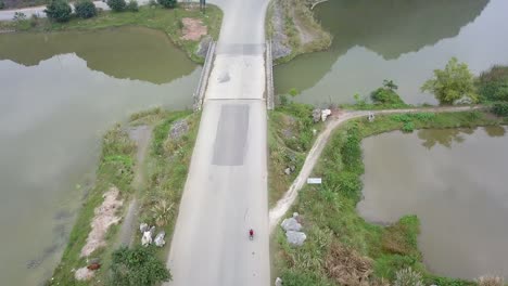 drone follow cam, motorbike in red shirt riding over small bridge with traffic and cliff