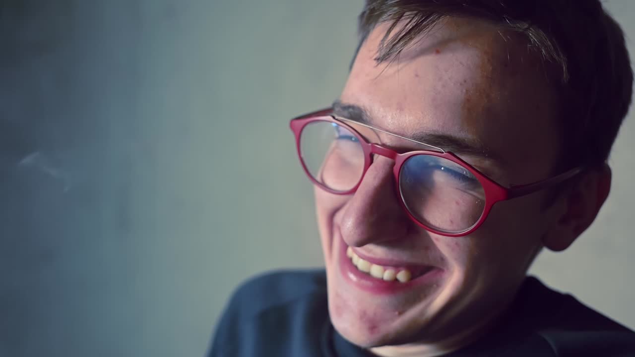 Young high man in red glasses vaping and smile indoor. Close up shot. Slow motion