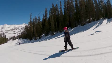 female snowboarder riding goofy down colorado ski resort on a bluebird day