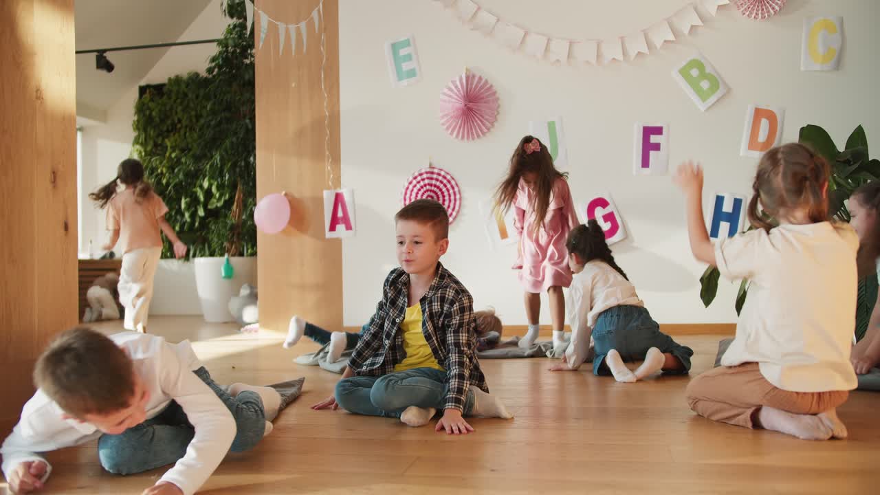 Happy preschool children have fun and rejoice during recess in a club preparing children for school. The happy children rejoice and have fun against the background of a wall with English letters in a club for preparing children for school
