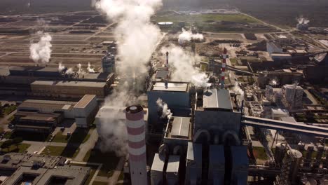 massive amount of steam ejected into air in huge factory facilities, aerial drone view