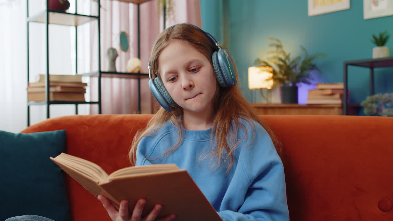 Ragazza preadolescente felice con le cuffie che legge un libro, sfoglia le pagine, sorride e si gode l'istruzione letteraria.