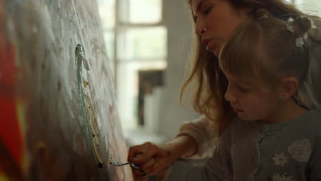 creative woman painter teaching little artist indoors. girl drawing on canvas.