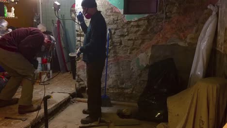 wide time lapse of two workers doing concrete demolition in a basement