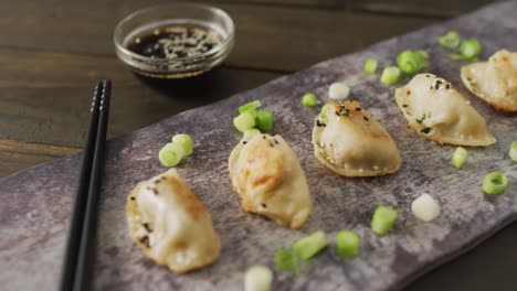 composition of plate with gyoza dumplings and soy sauce with chopsticks on wooden background