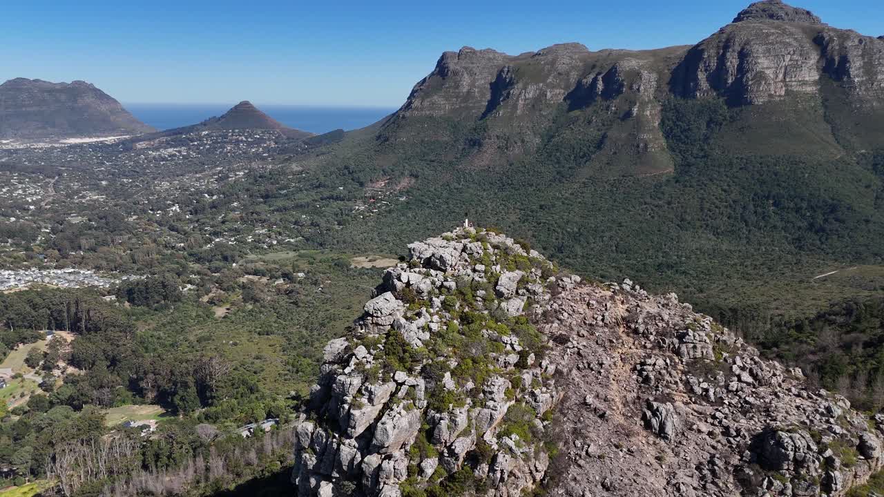 Aerial panoramic view of Cape Town, South Africa, with the Atlantic Ocean in the background, mountain peaks, and a valley below covered in lush green forest