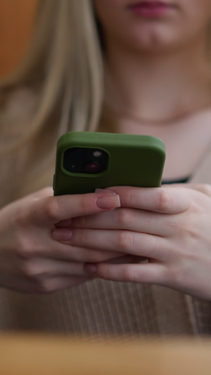 primer plano de una joven que opera un iphone con caja verde mientras está sentada en una mesa de madera, sus manos están enfocadas en la pantalla, mostrando atención a los detalles en un entorno relajado