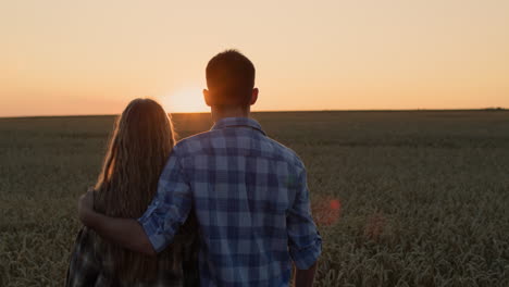 una pareja feliz admirando la puesta de sol sobre un campo de trigo.