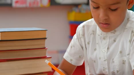 Vista-Frontal-De-Un-Atento-Colegial-Asiático-Estudiando-En-El-Escritorio-Del-Aula-En-La-Escuela-4k