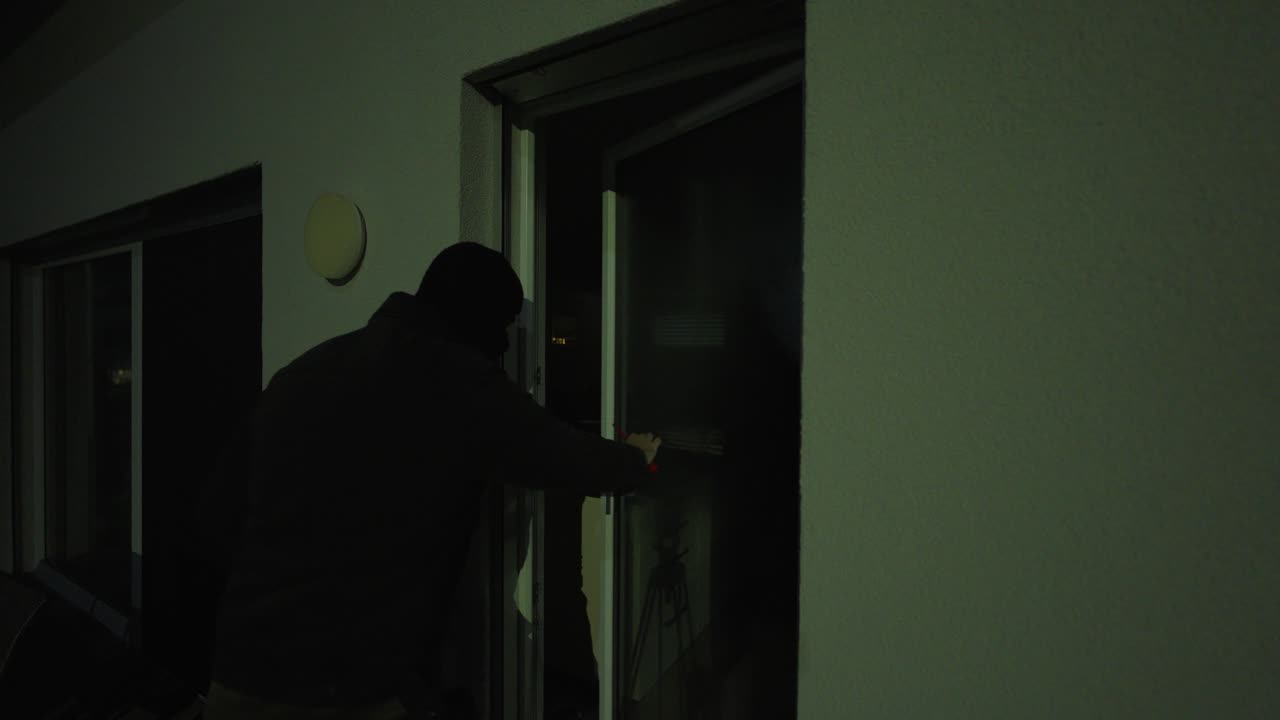 夜、フードを被った侵入者が外からパティオの引き戸を開けようとしているクローズアップ。緊迫感のあるホームセキュリティと強盗のコンセプト。