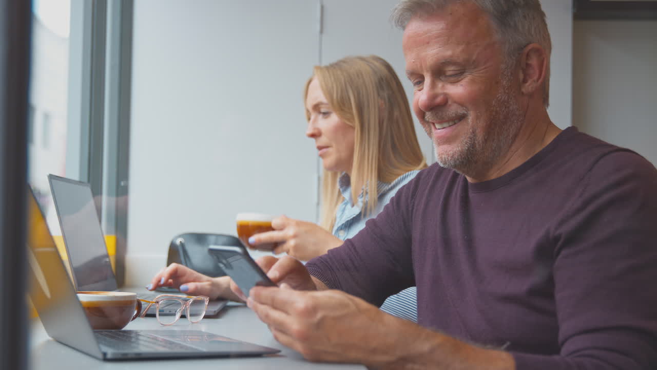 clienti in una finestra di un caffè che lavorano su laptop e navigano sul cellulare