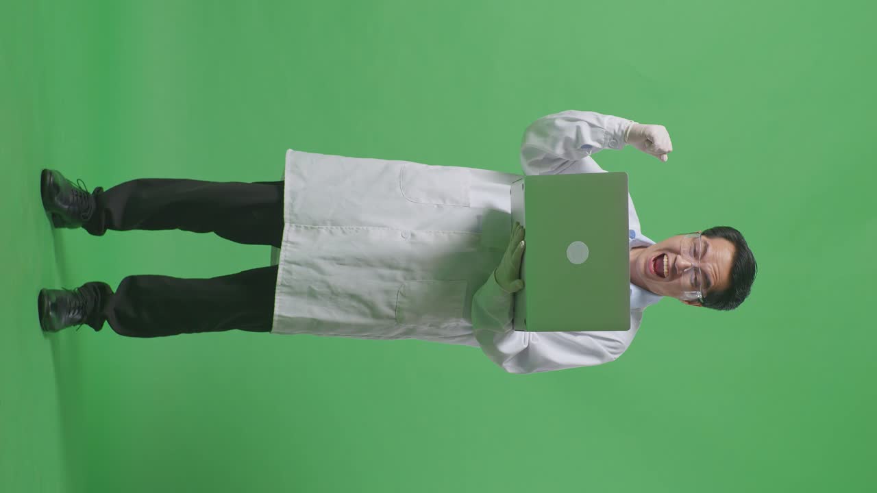 cuerpo lleno de científico hombre asiático mirando una computadora portátil y gritando meta celebrando mientras estaba de pie en el fondo de la pantalla verde en el laboratorio