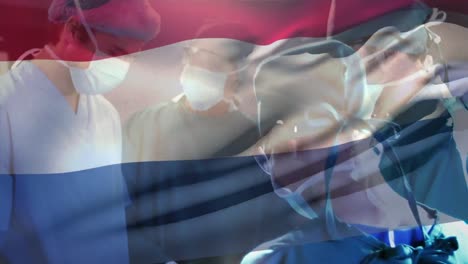 Animation-of-waving-netherlands-flag-over-team-of-diverse-surgeons-performing-operation-at-hospital