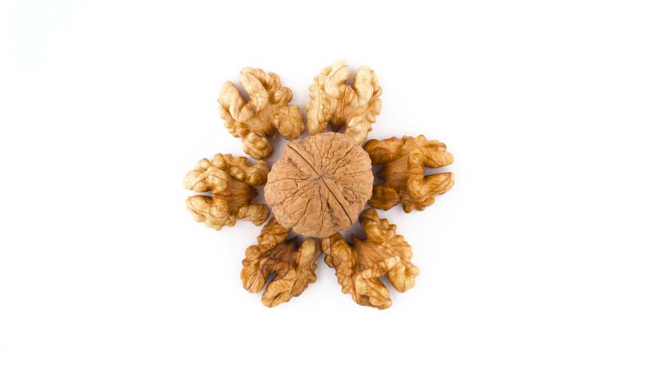 Top view from above of a circle shaped walnuts without the shell and one hazelnut in the shell in the center. Rotating on the turntable isolated on the white background. Close-up. Macro.