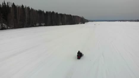 tracking aerial shot of a man driving his snowmobile on indalsalven in timra, sundsvall, sweden.