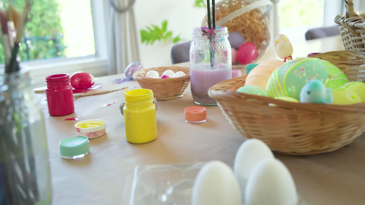 Camera is panning right across craft table, revealing painted eggs and brushes for Easter
