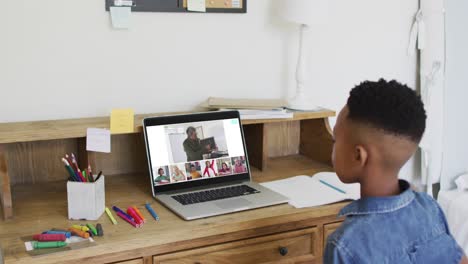 Schoolboy-using-laptop-for-online-lesson-at-home,-with-diverse-teacher-and-class-on-screen
