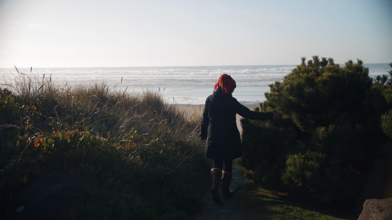 filmati 4k al rallentatore di una donna che cammina da sola verso la spiaggia mentre il tramonto tra le dune di sabbia