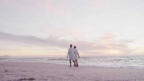 back view of hispanic senior couple walking on beach at sunset