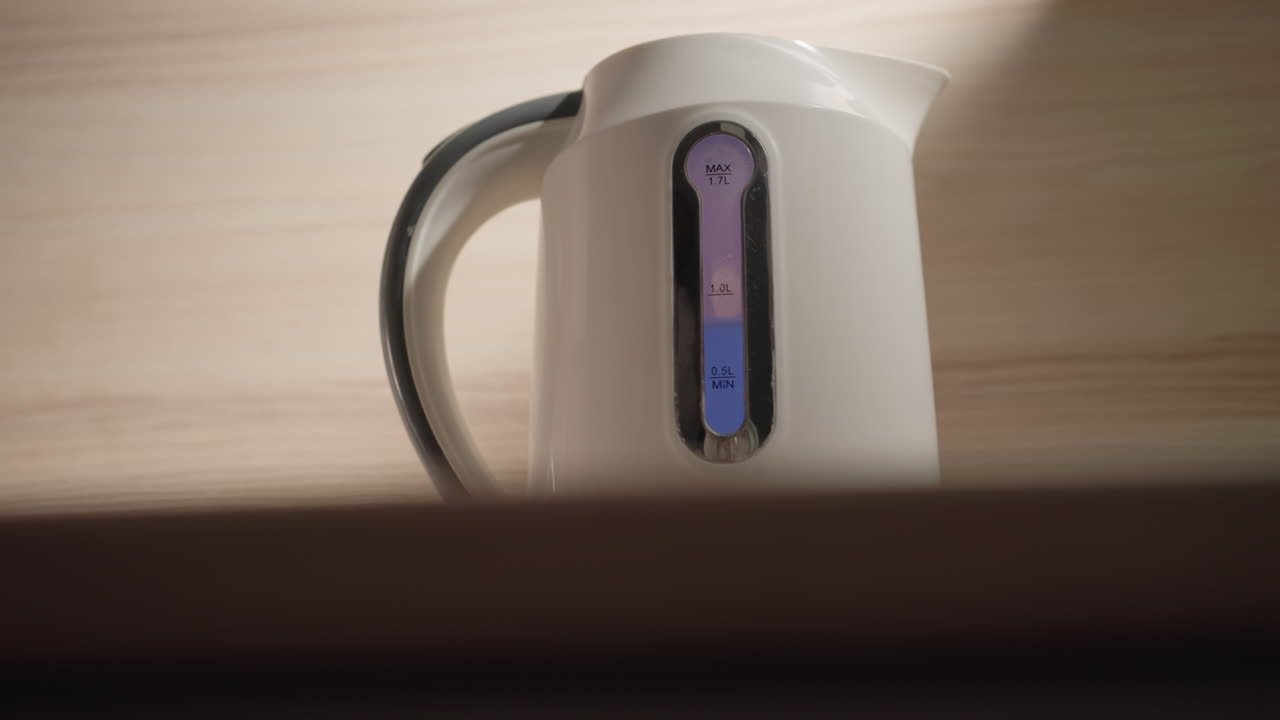 Close-up of electric kettle placed on countertop with visible water level indicator, soft light illuminating sleek design in minimalist kitchen environment. Clean lines and modern simplicity