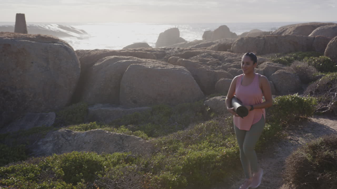 Walking along rocky coastline, mature asian woman holding spa towel, enjoying nature, copy space