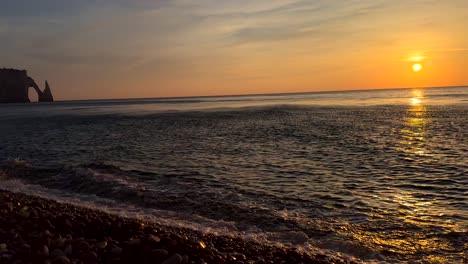 Panorama-Show-Mit-Bis-Zu-Den-Wellen-Reichenden-Meereswellen-Am-Kiesstrand-Und-Den-Berühmten-Felsbögen-Von-Etretat-Im-Hintergrund-Bei-Goldenem-Sonnenuntergang-–-Schwenkaufnahme