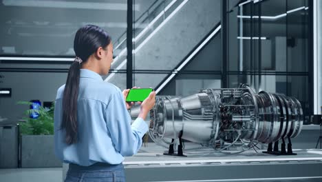 woman using green screen phone to photograph jet engine model in modern office