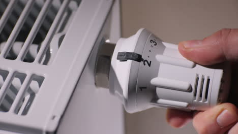 the male hand adjusts the temperature level on the thermostat of the heating radiator