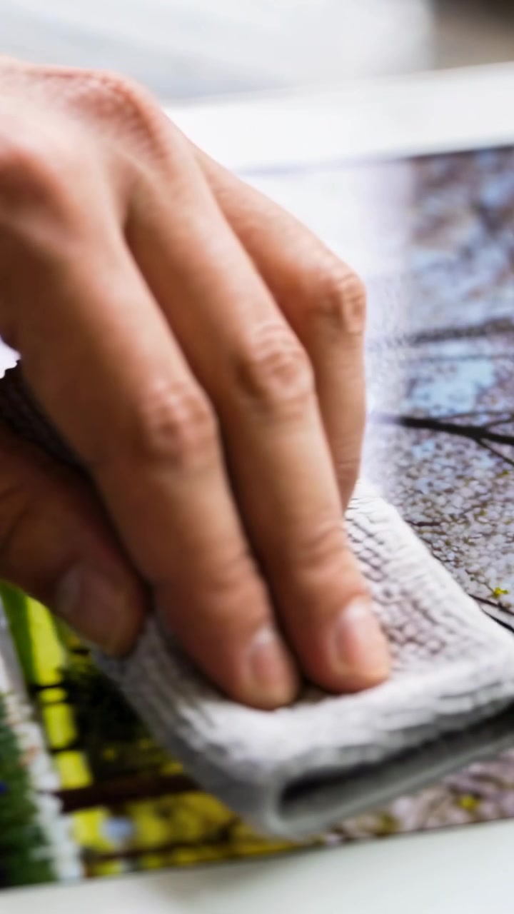 Vertical video: Wiping right hand placing microfiber cloth on table, cleaning glossy park print