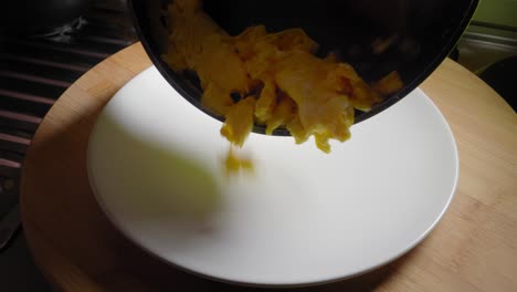 person is pouring scrambled eggs from a frying pan onto a plate