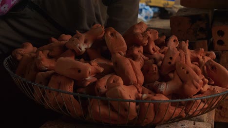 A-Thanh-Ha-artisan-stacks-freshly-fired-clay-flutes-of-animal-figures-in-a-metal-basket,-showcasing-traditional-craftsmanship-and-cultural-heritage