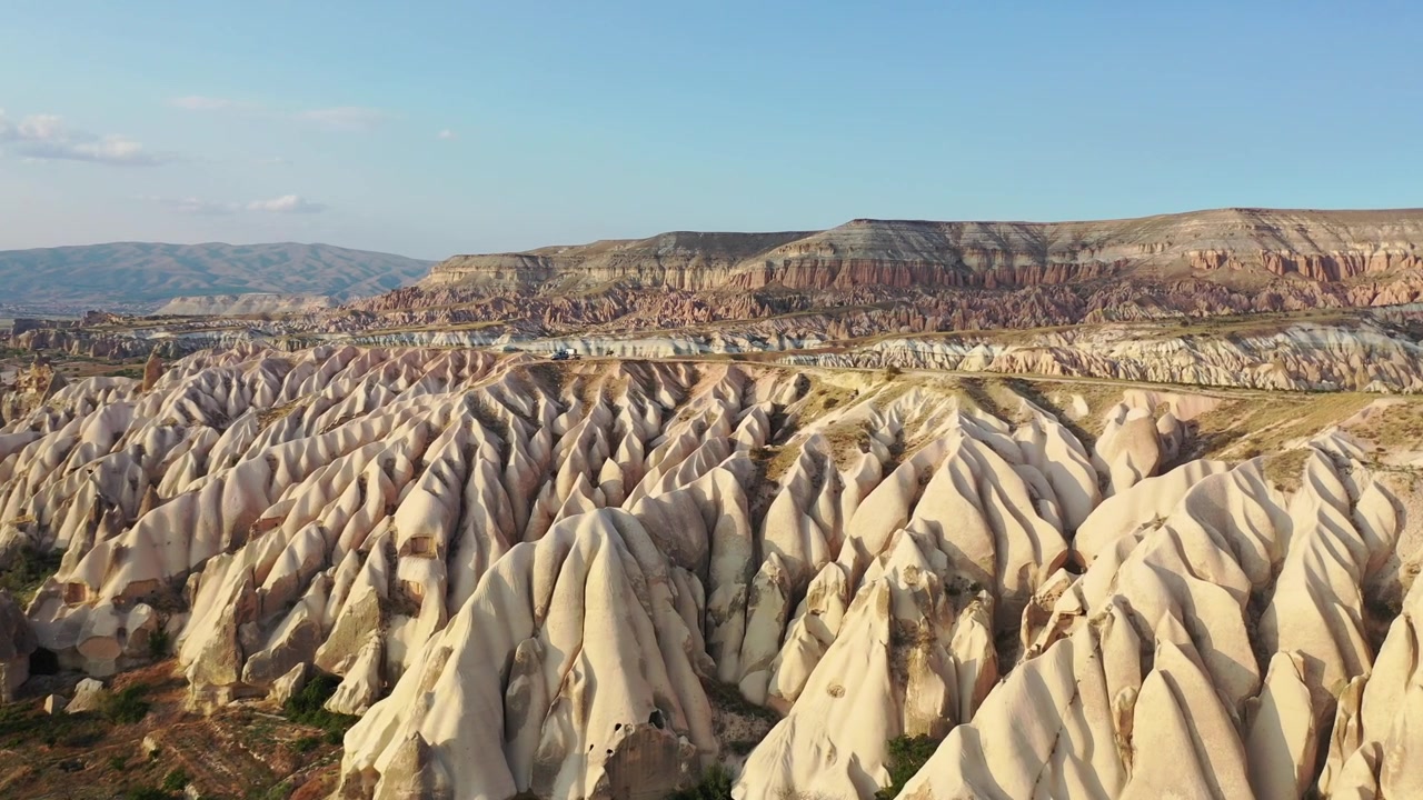 Vista panoramica aerea con drone di formazioni rocciose bianche, camini delle fate conici e montagne di tufo dalla cima piatta nella Valle delle Rose, Cappadocia, Nevsehir, Turchia, sotto un cielo azzurro e limpido.